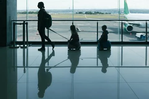 A mother pulls two children on small ride-on luggage through airport termin.. Stock Photos