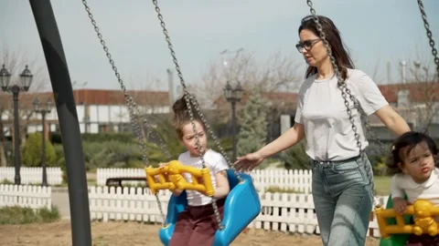 Mother Pushing Her Two Daughters on Swings Stock Footage 306732425