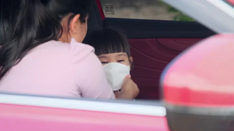 Mother puts on a face mask for her daughter to sit in the car .New normal. 스톡 동영상 172540149