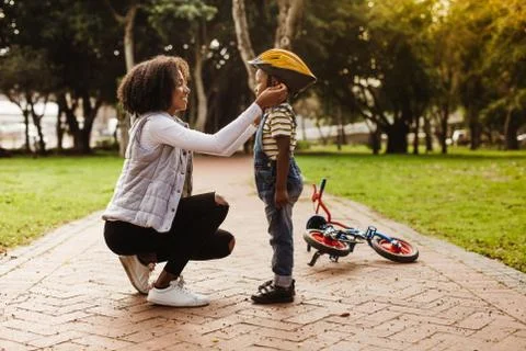 Mother puts her son protective helmet for riding bike Stock Photos