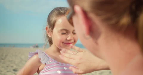 Mother puts sunscreen on her daughter's face while sitting on beach in summer. Stock Footage 175197301
