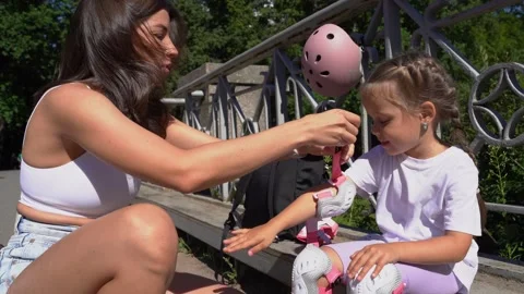 Mother putting on inline skates rollers elbow protection to daughter child in Stock Footage 240582538