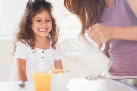 Mother putting milk in the cereal of his daughter Stock Photos