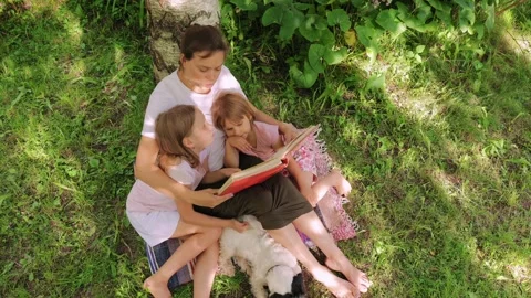 Mother reading a book to daughters in a summer garden setting Stock Footage 297761160