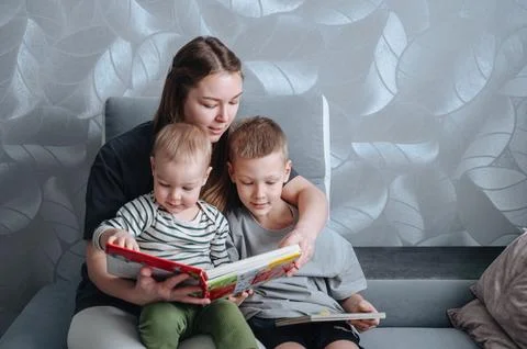 Mother reading a book to two small children while sitting in chair, family .. Stock Photos