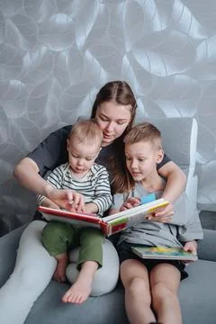 Mother reading a book to two small children while sitting in chair, family .. Stock Photos