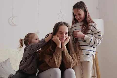 A mother relaxes on a couch while her two children play with her long hair. The Stock Footage 336461225