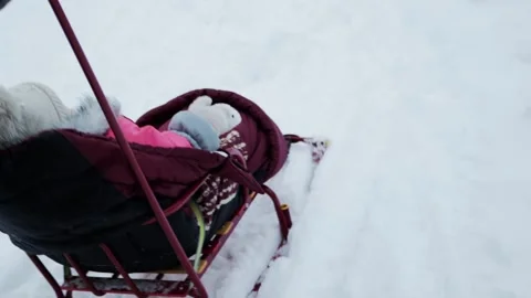 A mother rides her 1-2 year old daughter on a sled down a mountain in the snow Vídeo Stock 254065089