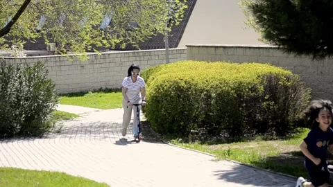 Mother riding a scooter in a park while her son runs Stock Footage 307100106