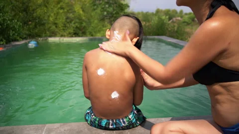Mother Rubs Sunscreen Onto Son's Back at Pool Edge Stock Footage 343359087