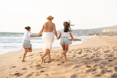 Mother running with two daughters on a sandy beach Photos