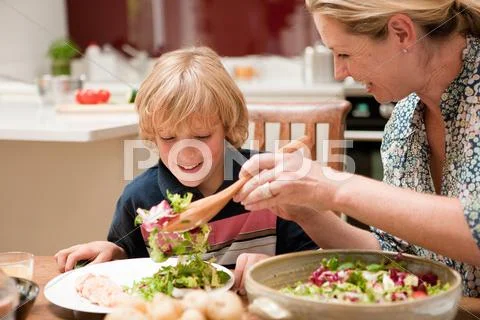 Mother Serving Salad To Son At Dining Table