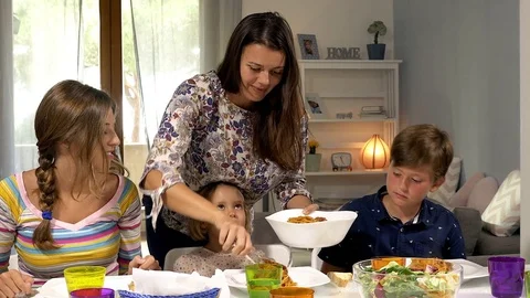 Mother serving spaghetti with tomato sauce to children at the table kissing d Stock Footage