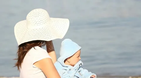 Mother setting her hat and caressing her baby at the littoral Stock Footage 12272276