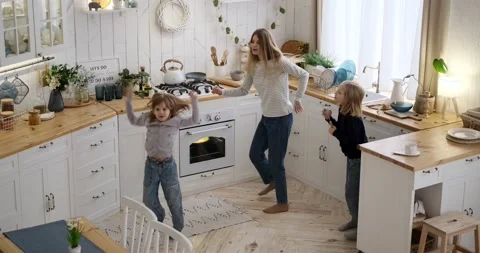 Mother singing and dancing cheerfully with daughters in kitchen Stock Footage 239453961