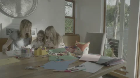 A mother sits with her two daughters working on arts and crafts. Stock Footage 68353524