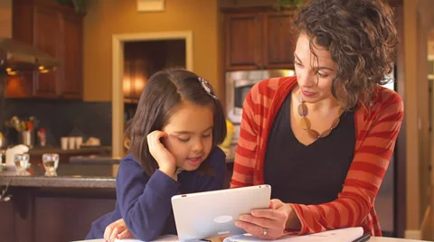 A mother sits at the kitchen table and assists her young daughter with her Video stock 34003413