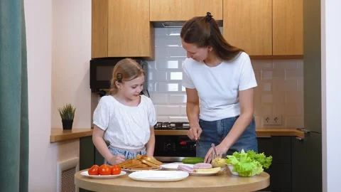 Mother slicing cucumber while preparing sandwiches with daughter in kitchen Stock Footage 317815906