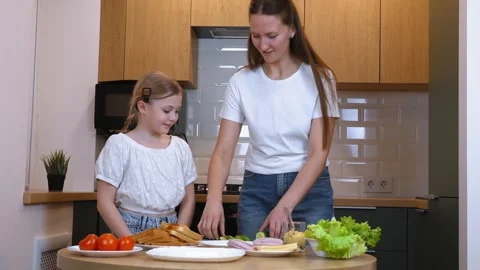 Mother slicing cucumber while preparing sandwiches with daughter in kitchen Stock Footage 317815914