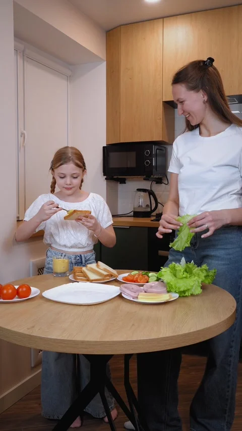 Mother slicing cucumber while preparing sandwiches with daughter in kitchen Stock Footage 317819606