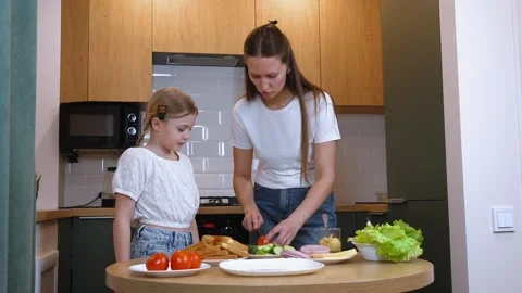 Mother slicing cucumber while preparing sandwiches with daughter in kitchen Stock Footage 317820290