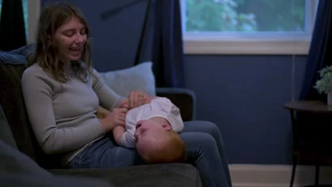 Mother smiles warmly while playing with her young child, who lies on her lap on Stock Footage 289677971