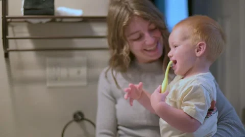 Mother smiles warmly while supervising her toddler brushing teeth with yellow Stockbeeldmateriaal 289678008