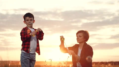 Mother with son blows soap bubbles in field under bright sunset low angle shot Stock Footage 255071538