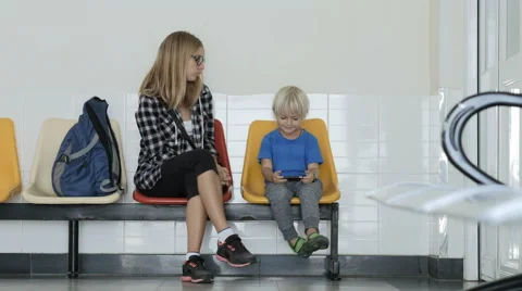 Mother with son sitting in queue to doctor in clinic playing game on phone. Stock Footage 61876231