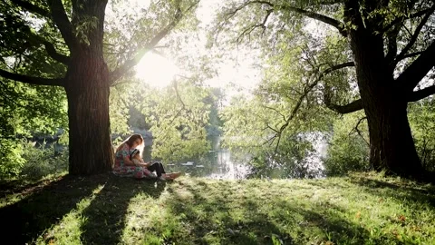Mother with son sitting under the tree in the shadow on lawn on summer day Stock Footage 269444289
