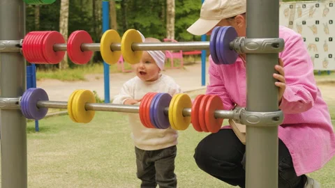 A mother spends time with her young child on the playground in the park Stock Footage 234320616