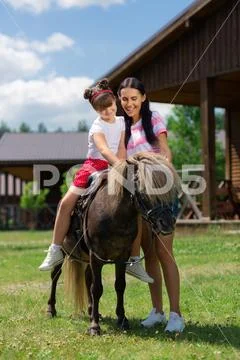 Mother standing near daughter sitting on horse for the first time Stock Photos