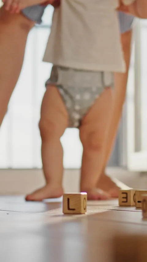Mother steadies her babys first steps on a smooth floor holding the childs p Stock Footage 341284556