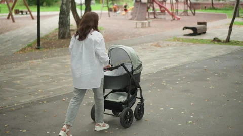 Mother with stroller proceeding through lively community space. Woman pushing Video stock 346395882