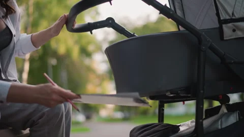 Mother studying paperwork beside stroller in park setting. Parent reviewing Video stock 346383392
