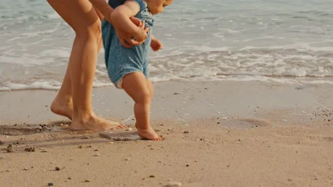 Mother is support her child to do the first steps on beach sand Stock Footage 196744879