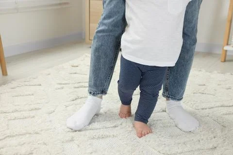 Mother supporting her son while he learning to walk on carpet indoors, clos.. Foto stock