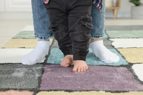 Mother supporting her son while he learning to walk on carpet indoors, closeu Foto stock