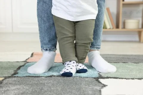 Mother supporting her son while he learning to walk on carpet indoors, closeu Foto stock
