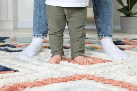 Mother supporting her son while he learning to walk on carpet indoors, closeu 写真素材