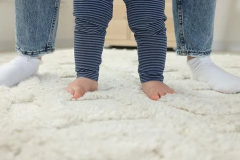 Mother supporting her son while he learning to walk on carpet indoors, closeu Foto stock