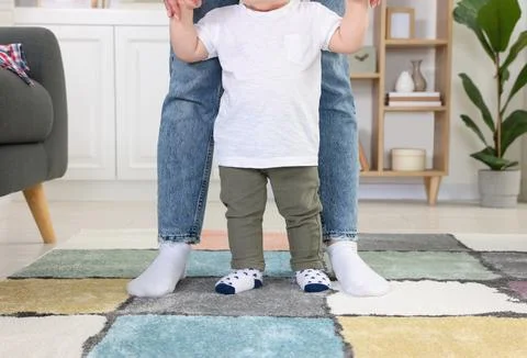 Mother supporting her son while he learning to walk on carpet indoors, closeu Foto stock