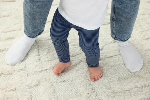 Mother supporting her son while he learning to walk on carpet, closeup 写真素材