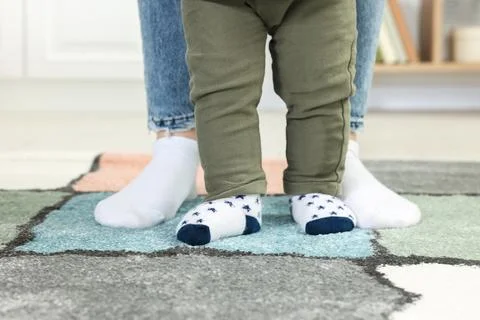 Mother supporting her son while he learning to walk on carpet indoors, closeu Foto stock