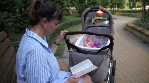Mother sways baby in a stroller while reading 库存影片 227874822