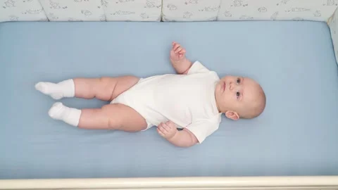 Mother taking pacifier from cute baby's mouth in crib. Adorable infant lying in Vídeos de archivo 344692239