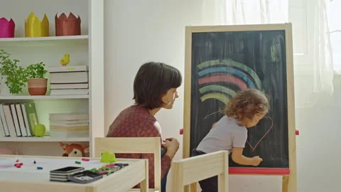 Mother teaching child to write letters on chalkboard at home. Stock Footage 252122470