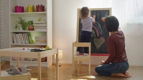 Mother teaching child to write letters on chalkboard at home. Stock Footage 252125311