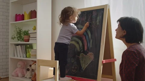 Mother teaching child to write letters on chalkboard at home. Stock Footage 252125529
