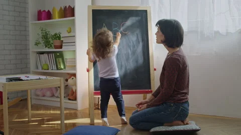 Mother teaching child to write letters on chalkboard at home. Stock Footage 252127320